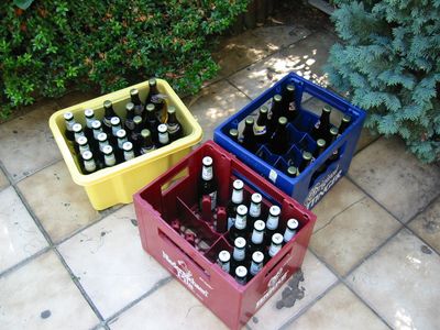 Drei Getränkekisten voller Flaschen auf einer gefliesten Terrasse.