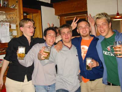 Fünf Freunde in einer Küche prosten mit Biergläsern in die Kamera.