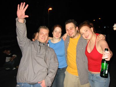 Vier Freunde Arm in Arm bei Nacht, einer winkt in die Kamera.