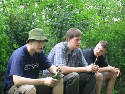 Drei junge Männer mit Bierflaschen sitzen im Grünen.