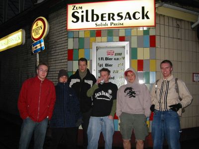 Sechs Personen vor dem Eingang einer Kneipe mit Leuchtschild, bei Nacht.