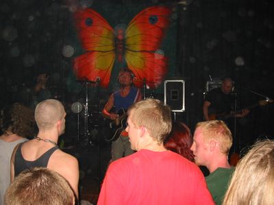 Konzert in einem Club, vor der Bühne mit großem Schmetterling stehen Zuschauer.