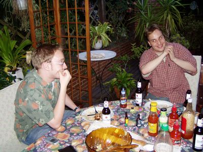 Zwei Männer an einem gedeckten Tisch im Garten unter einem Rankgitter.
